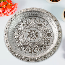 A silver-colored plastic pooja thali with embossed patterns, surrounded by orange flowers and two white containers on a