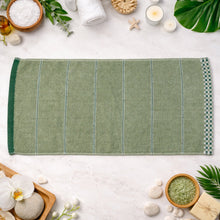 A green striped cotton hand towel lies flat on a white surface, surrounded by various spa and bath accessories.