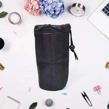 A navy blue drawstring pouch with vertical stripes stands upright on a white surface, surrounded by office supplies and