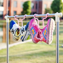 Two pairs of colorful athletic shoes hang from pink plastic racks on a metal clothesline outdoors.