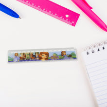 A Sofia the First ruler on a white desk next to a spiral notebook, with a blue pen and pink ruler in the background.