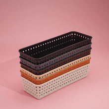 A stack of six rectangular plastic baskets in different colors on a pink background.