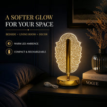 A glowing feather-shaped crystal table lamp on a bedside table with books, a vase, and a USB cable.