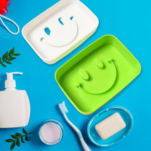 A green and a white soap dish, both with smiley face designs, surrounded by bathroom items on a blue background.