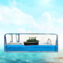 A clear rectangular liquid motion paperweight with a green ship and iceberg floats in blue liquid against a blue sky