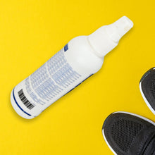 A white and blue bottle of shoe and sock deodorant lies diagonally on a bright yellow background, with the toes of black