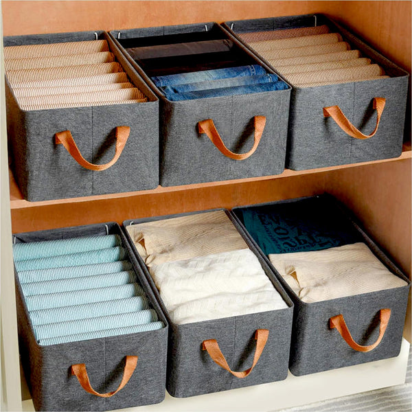 Six grey fabric storage boxes with brown handles, filled with folded clothes, on light wooden shelves.