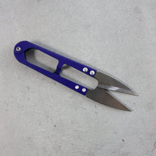 A pair of blue handle thread snips with silver blades lies on a gray concrete surface.