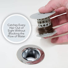 A hand holds the white silicone drain hair catcher with brown hair wrapped around it, next to a clean chrome drain, with