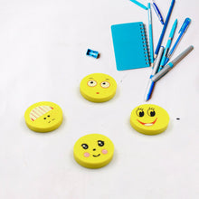 Four yellow round emoji erasers are scattered on a white surface with blue school supplies in the background.