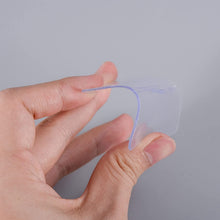 A hand holds and bends a clear, flexible adhesive square, highlighting its pliability.