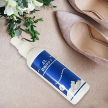 A white and blue bottle of shoe and sock deodorant lies on a light brown textured surface next to a pair of nude high heels