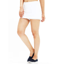 A woman models a white layered hip skirt with shorts and dark blue slip-on shoes, walking with her left leg forward.