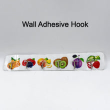 A white adhesive wall hook strip with fruit designs is centered on a plain white background with the text 