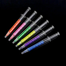 Six syringe highlighters in various colors (orange, pink, green, yellow, purple, blue) arranged on a black surface.