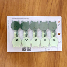 Ten cat-shaped wall hooks, five dark green and five light green, packaged in clear plastic on a wooden surface.