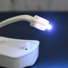 Close-up of the white motion sensor toilet light's flexible arm and glowing blue light on a dark blue surface.