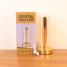 A gold and clear crystal table lamp, its packaging, and a white USB charging cable on a wooden surface.