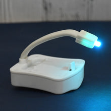 White motion sensor toilet light with a flexible arm, emitting a blue-green glow, on a dark blue surface.