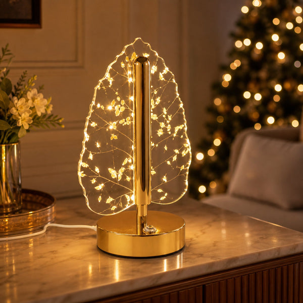 A golden crystal leaf LED table lamp illuminates a marble table with a blurred Christmas tree in the background.