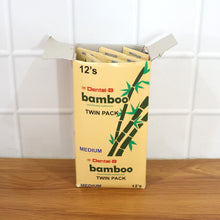 An open cardboard box filled with multiple twin packs of bamboo toothbrushes, against a white tiled wall.