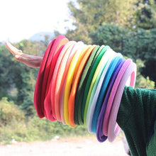 A hand holding a stack of colorful soft fabric toilet seat covers against a blurry outdoor background.