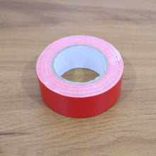 A single roll of red tape on a wooden surface.
