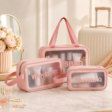 Three pink waterproof travel bags with clear panels sit on a white marble table with a mirror and flowers.
