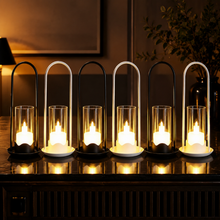 Six flameless LED lanterns with glass cylinders and arched metal handles, three black and three white, glowing warmly on a