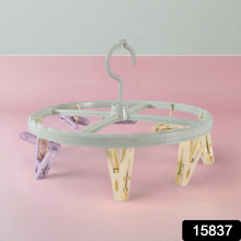 A light blue circular drying rack with purple and yellow clips stands on a pink and grey background.