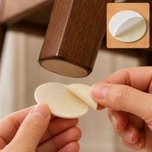 Hands peeling a round beige adhesive pad from its backing, about to apply it to a furniture leg.