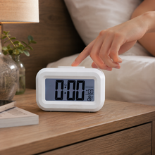 A hand reaches to press the top button of a white digital clock displaying 0:00 and 28 degrees Celsius.