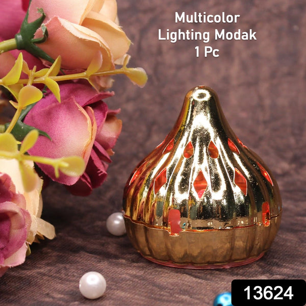 A gold modak-shaped LED light with red diamond cutouts is surrounded by pink flowers and white pearls.