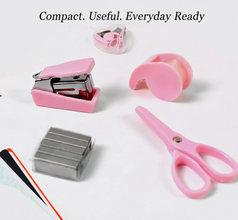 A pink mini stapler, tape dispenser, scissors, and a box of staples on a white surface with text 