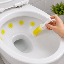 A hand applies a yellow flower-shaped gel stamp to the inside of a white toilet bowl.