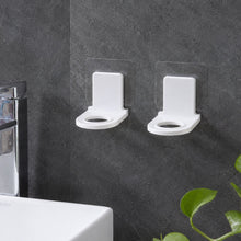 Two white plastic bottle holders with clear adhesive pads lying on a light gray tiled floor beside a white bathtub.