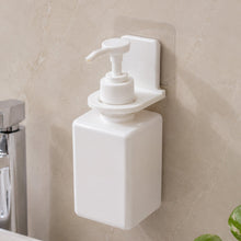 Two white plastic bottle holders on a gray tiled wall, one holding a loofah and the other a white pump bottle.
