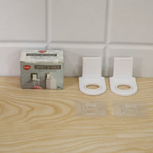 A product box and two white plastic bottle holders with their clear adhesive pads are arranged on a light wooden surface.