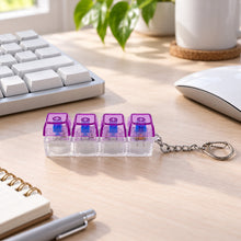 A four-key keyboard switch keychain on a wooden desk with a white keyboard, mouse, and notebook in the background.