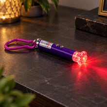 A purple laser pointer keychain with a clear flower cap illuminates a red light pattern on a dark surface.