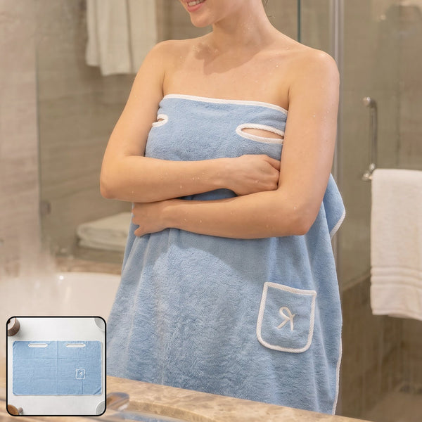 Woman wearing a light blue wearable bath towel with a white trim and a small pocket, standing in a bathroom.
