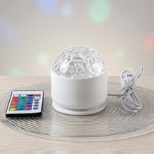A white LED projection light with a clear textured dome and a remote control resting on a clear glass plate.