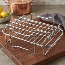 A shiny metal air fryer rack sits on a dark wooden cutting board, with a copper pot and lemons in the background.