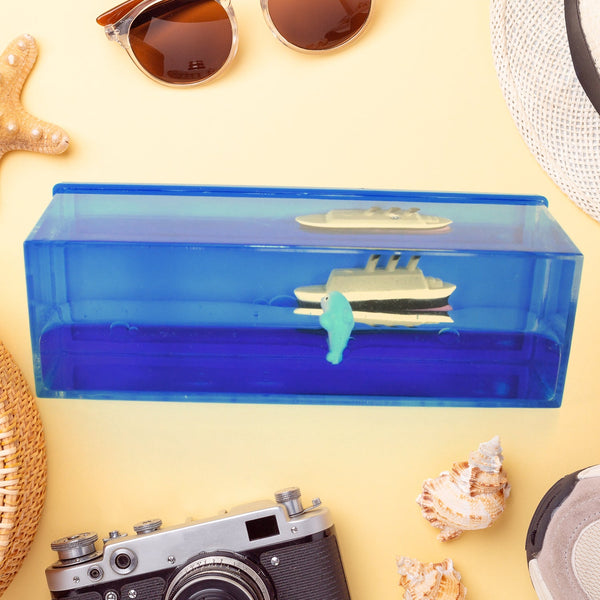A clear rectangular acrylic box with blue liquid, a white and gray ship, and a small white dolphin inside, surrounded by