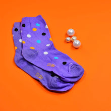 A pair of purple crew socks with various colored polka dots and small white pearls on an orange surface.