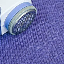 Close-up of a blue and white lint remover removing fuzz from a purple knitted fabric.