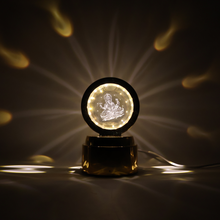 A golden lamp with a glowing Ganesha crystal projects starburst patterns onto a dark background, with a white cable.