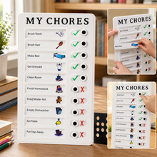 White 'MY CHORES' checklist board with green checkmarks and red X's on a wooden desk with books and a plant.
