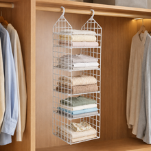 White 5-layer plastic hanging closet organizer filled with folded clothes in a wooden closet.