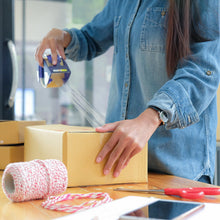A person using a blue and white tape dispenser to seal a brown cardboard box with transparent tape.